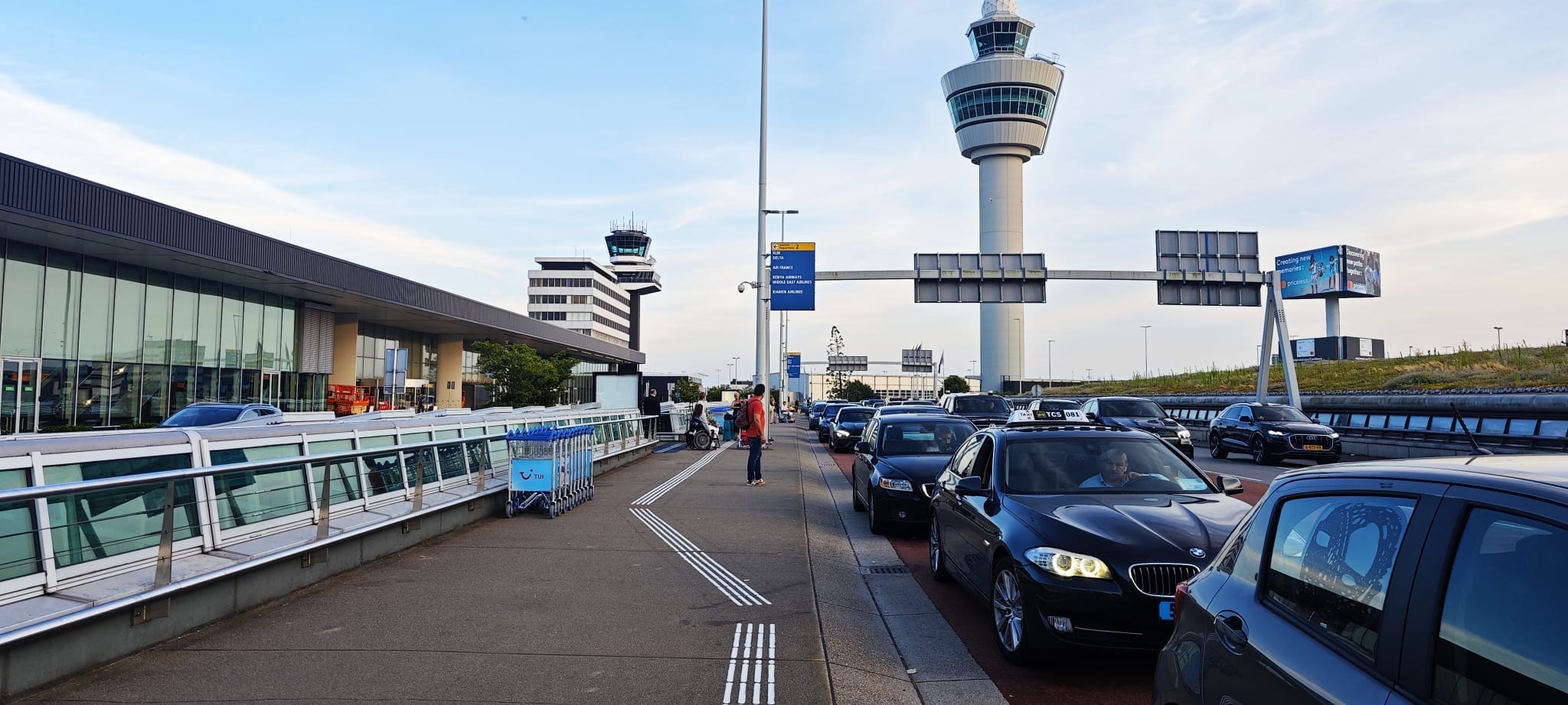 Taxi-opstelplaats bij Schiphol. Op de achtergrond staat de toren van de luchtverkeersleiding. Langs de taxi’s loopt een geleidelijn.